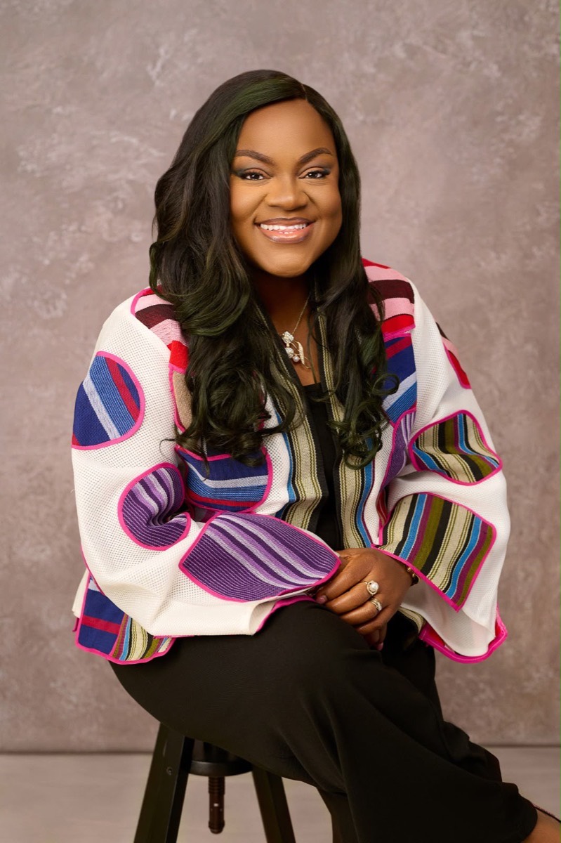 Busayo Disu seated in a colourful striped African print jacket, smiling