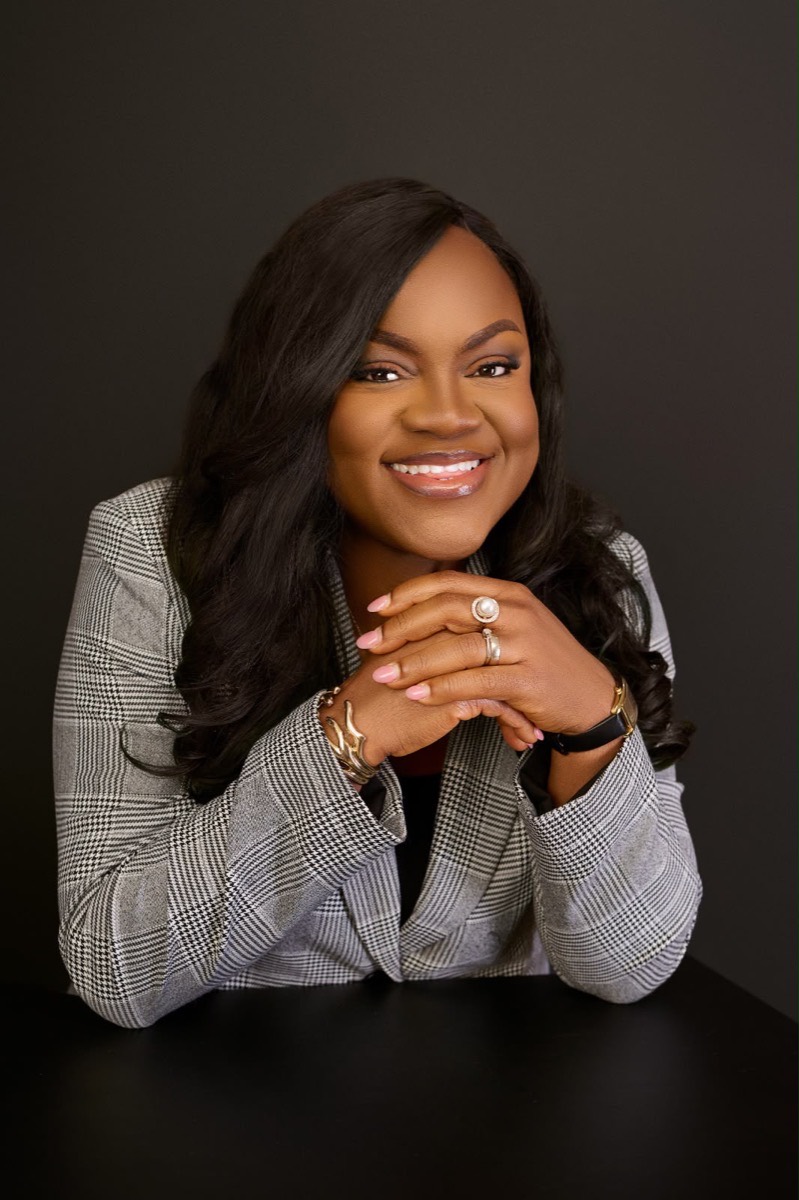 Busayo Disu in a grey houndstooth blazer, leaning on a table