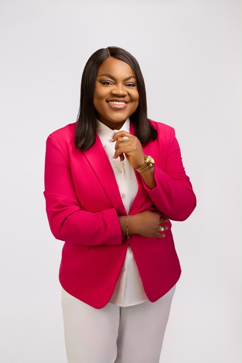 Busayo Disu in a bright pink blazer, hand resting near her chin